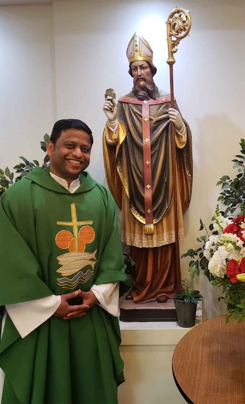 Fr Pinto standing next to a statue of St Patrick